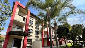 A multi-story building with balconies, a covered outdoor seating area, and a well-maintained lawn.