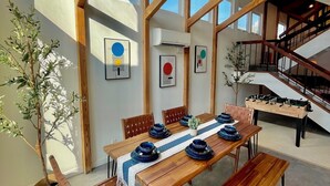 A dining area with a wooden table set for four, surrounded by chairs, in a room with exposed wooden beams and a staircase. - Naples Island rooftop deck/bbq AC & 2 car garage (Long Beach)