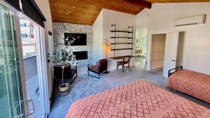 A room with a stone wall, a fireplace, a TV, a bed, a chair, and a wooden ceiling. - Naples Island rooftop deck/bbq AC & 2 car garage (Long Beach)