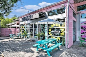 A market with a pink exterior, glass storefront, and outdoor seating area with turquoise benches. - "The Southern Pearl" - Cute 1bd/1ba in Park Circle (North Charleston)