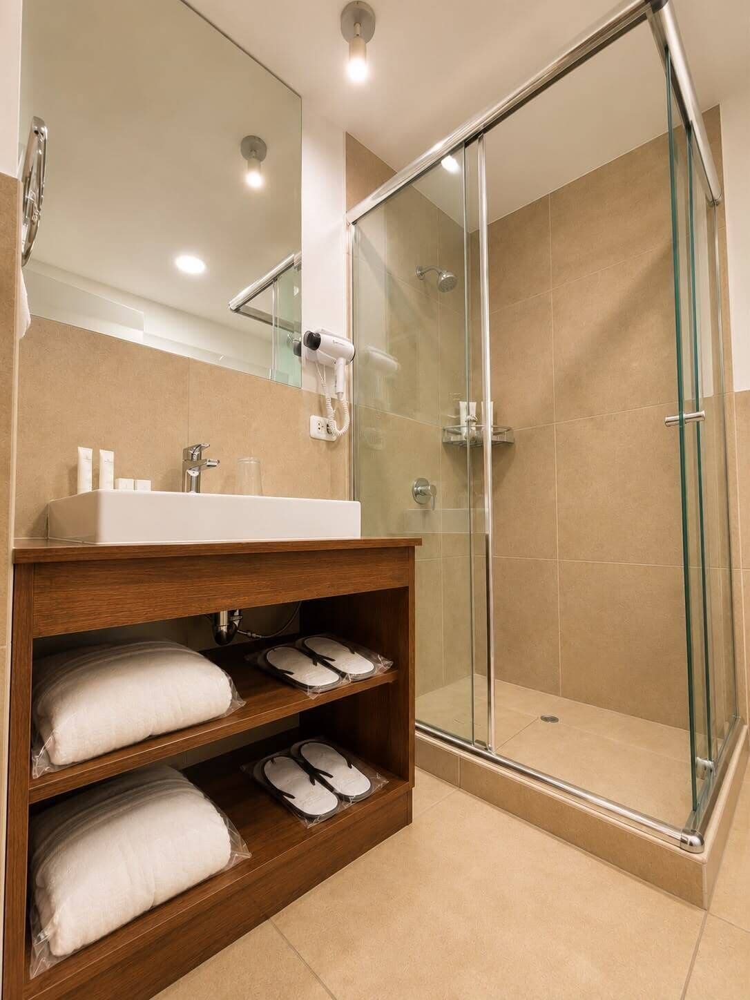 A modern bathroom with a glass-enclosed shower, a wooden vanity with towels, and a mirror above the sink.