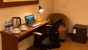 Habitación de hotel con escritorio de madera, una computadora portátil, cafetera, silla, minibar y unidad de aire acondicionado.