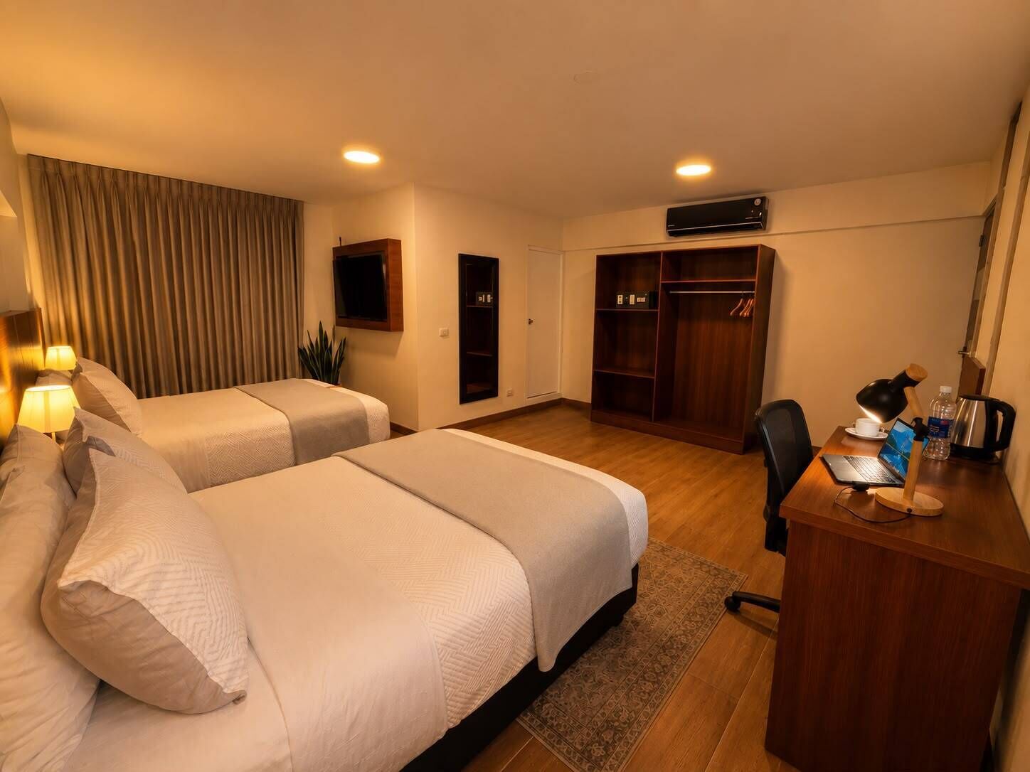 A hotel room with two beds, a desk with a laptop, a wardrobe, and a television.