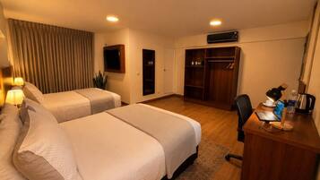 A hotel room with two beds, a desk with a laptop, a wardrobe, and a television.