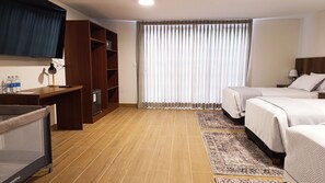 A hotel room with a wooden desk, a small refrigerator, a TV, a bed with two pillows, and a large window with curtains. - Casa Pucllana Miraflores - Hotel Boutique (Lima)