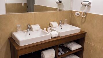 A bathroom with two sinks, a mirror, and a shelf with towels and slippers.