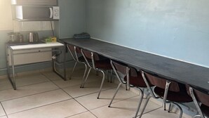 Een kamer met een lange tafel, stoelen, een magnetron, een waterkoker en een lijst met een afbeelding aan de muur.