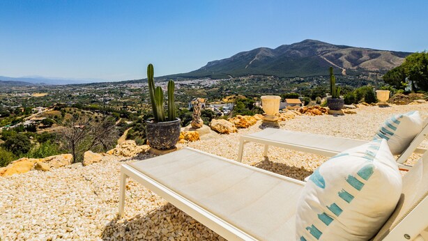 Terraza con vistas a un pueblo y montañas, con mobiliario exterior y plantas en macetas.