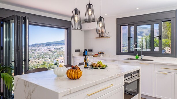 Une cuisine moderne dotée d’un grand îlot central, de meubles blancs, de poignées dorées et de luminaires suspendus.