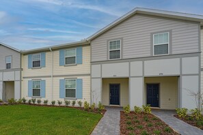 A row of townhouses with a front entrance, a small garden area, and a clear sky.