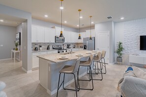 A modern kitchen with white cabinets, a central island with bar stools, stainless steel appliances, and pendant lighting.