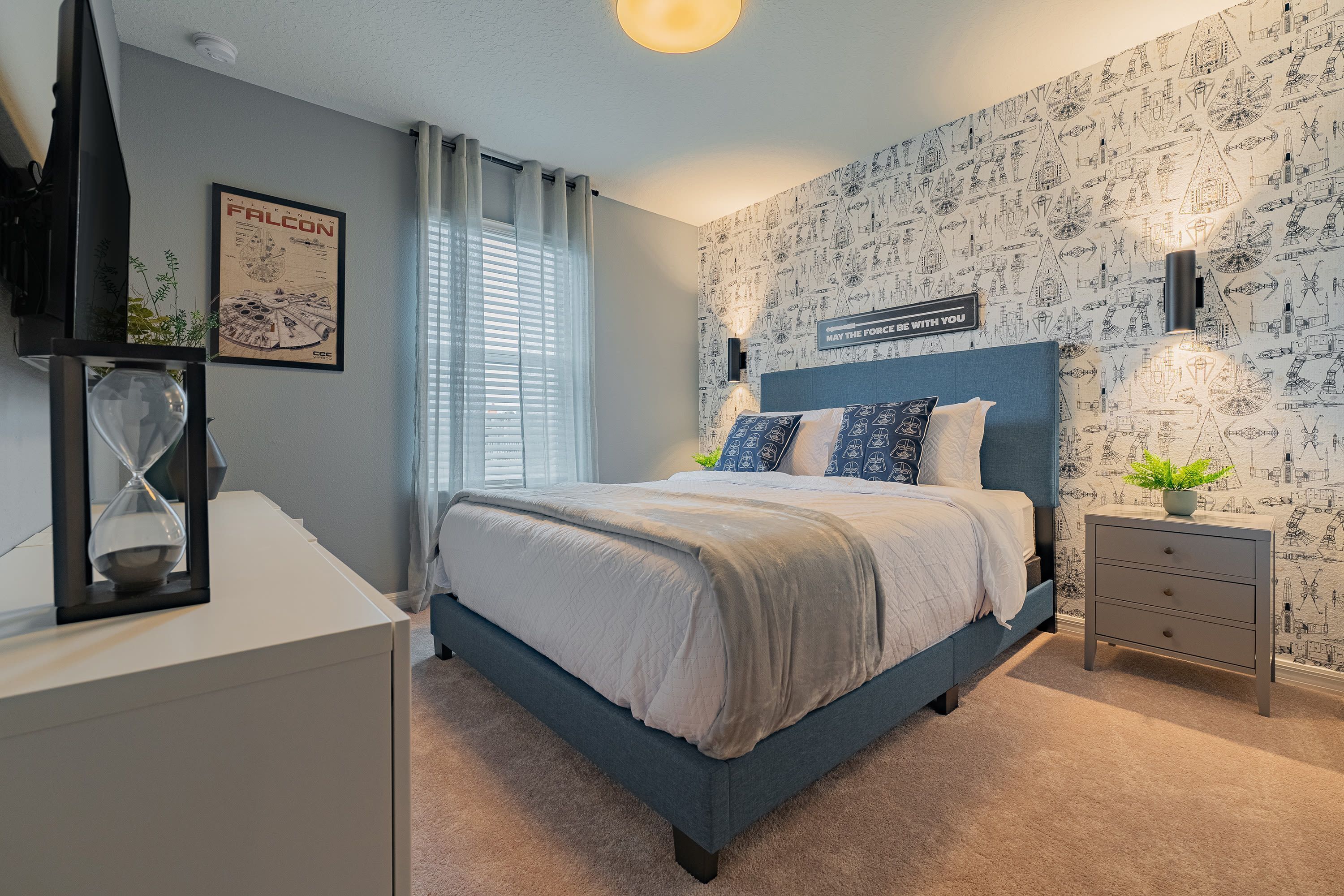 Une chambre à coucher comprenant un lit, une table de chevet, une commode, une horloge murale, une affiche encadrée et une fenêtre avec des rideaux.