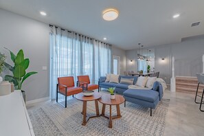 A modern living room with a sofa, two armchairs, a coffee table, and a dining area with a table and chairs.