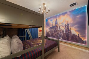 Una cama litera con un mural de temática de castillo, un candelabro y una colcha a rayas azul y roja.