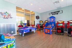 Una zona de juegos con varias máquinas de arcade, una mesa de billar y un simulador de baloncesto.