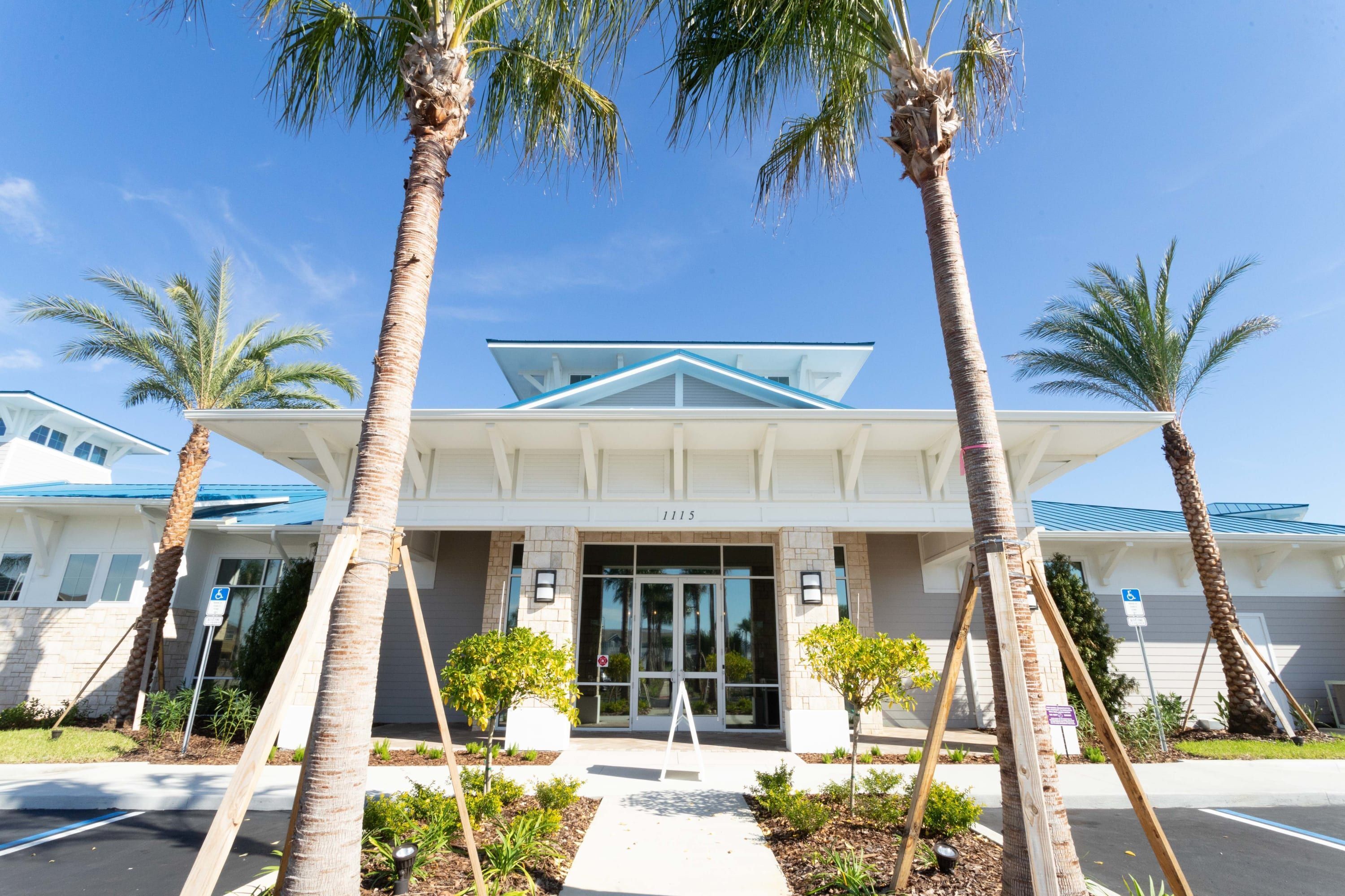 A hotel entrance with a white facade, palm trees, and a clear blue sky.