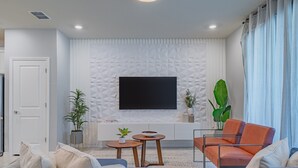 Ein modernes Wohnzimmer mit Flachbildfernseher, einer Couch, einem Couchtisch und Zimmerpflanzen.