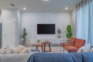 Un salon moderne avec un téléviseur à écran plat, un canapé, une table basse et des plantes décoratives.