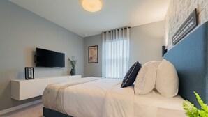 Ein modernes Schlafzimmer mit Bett, einem Wand-Fernseher, einem Nachttisch und einem Fenster mit Vorhängen.