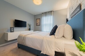 Une chambre à coucher moderne avec un lit, un téléviseur fixé au mur, une table de chevet et une fenêtre avec des rideaux.