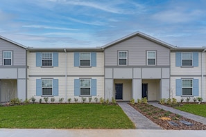 A modern multi-story residential building with a symmetrical facade, a central entrance, and a well-maintained lawn.