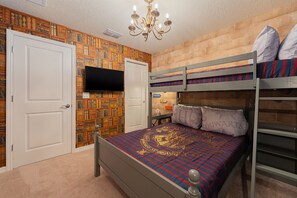 Une chambre à coucher avec un lit superposé, un téléviseur à écran plat, une bibliothèque et un lustre.