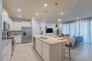 A modern kitchen with white cabinets, stainless steel appliances, a granite countertop, and pendant lighting.