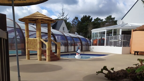 A pool area with a wooden play structure, a covered seating area, and a building with large windows.