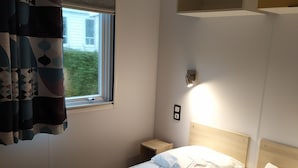 A hotel room with a bed, a bedside table, a wall-mounted air conditioner, and a window with curtains.