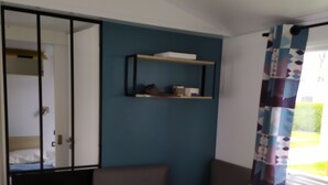 A room with a wooden table, a bench, a shelf with items, and a window with a curtain.