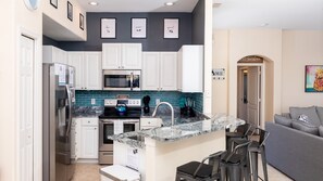 Una cocina compacta con armarios blancos, un salpicadero de azulejos azules y un refrigerador de acero inoxidable.