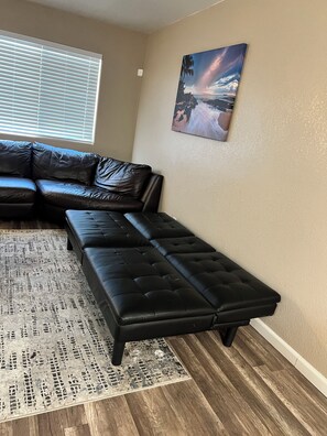 Un soggiorno con un divano componibile, una poltrona chaise-lounge, un tappeto decorato e un quadro appeso al muro.