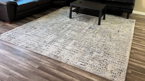 Ein Wohnzimmer mit einem Ecksofa, einem Couchtisch und einem gemusterten Teppich auf Holzboden.