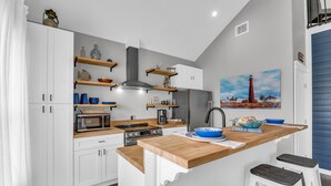 A modern kitchen with white cabinetry, wooden countertops, and a central island with stools.