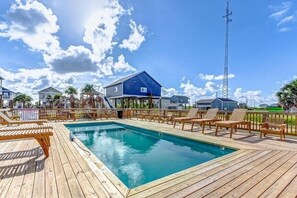Una terrazza in legno con piscina, sedie a sdraio e un edificio blu con antenna parabolica.