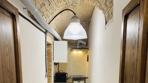 A narrow hallway with a herringbone-patterned floor, a kitchen area with a white tiled backsplash, and a hanging light fixture. - Loft in Pieno Centro Storico con Arredamenti di Design e Ingresso Indipendente (Rieti)