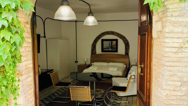 A room with a bed, a table, and chairs, an arched doorway, and hanging plants. - Loft in Pieno Centro Storico con Arredamenti di Design e Ingresso Indipendente (Rieti)