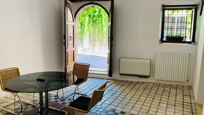 A room with a round glass table, two wicker chairs, a hanging light fixture, a door with a view of greenery, a window with bars, and a radiator. - Loft in Pieno Centro Storico con Arredamenti di Design e Ingresso Indipendente (Rieti)
