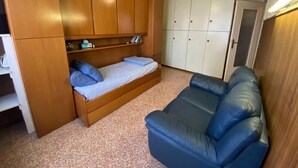 Une pièce de taille modeste comprenant un lit, un canapé bleu, des meubles en bois et une armoire.