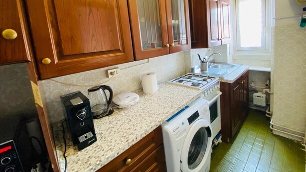 Une cuisine compacte avec des meubles en bois, un lave-linge, une machine à café et un évier.