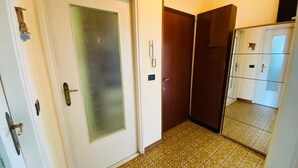 Un couloir avec une porte blanche dotée d’un panneau en verre dépoli, une porte en bois et un sol carrelé orné d’un motif géométrique.