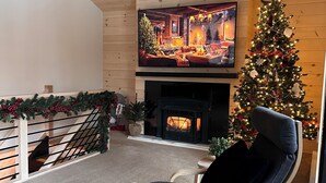 Una sala de estar acogedora con chimenea, un árbol de Navidad y un televisor mostrando una escena navideña.