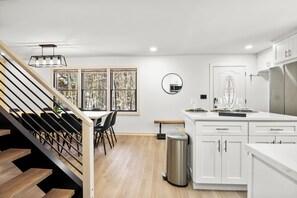 A modern kitchen with white cabinets, a stainless steel refrigerator, and a dining area with a wooden staircase. - Modern Cottage between Stratton and Mount Snow (Wardsboro)