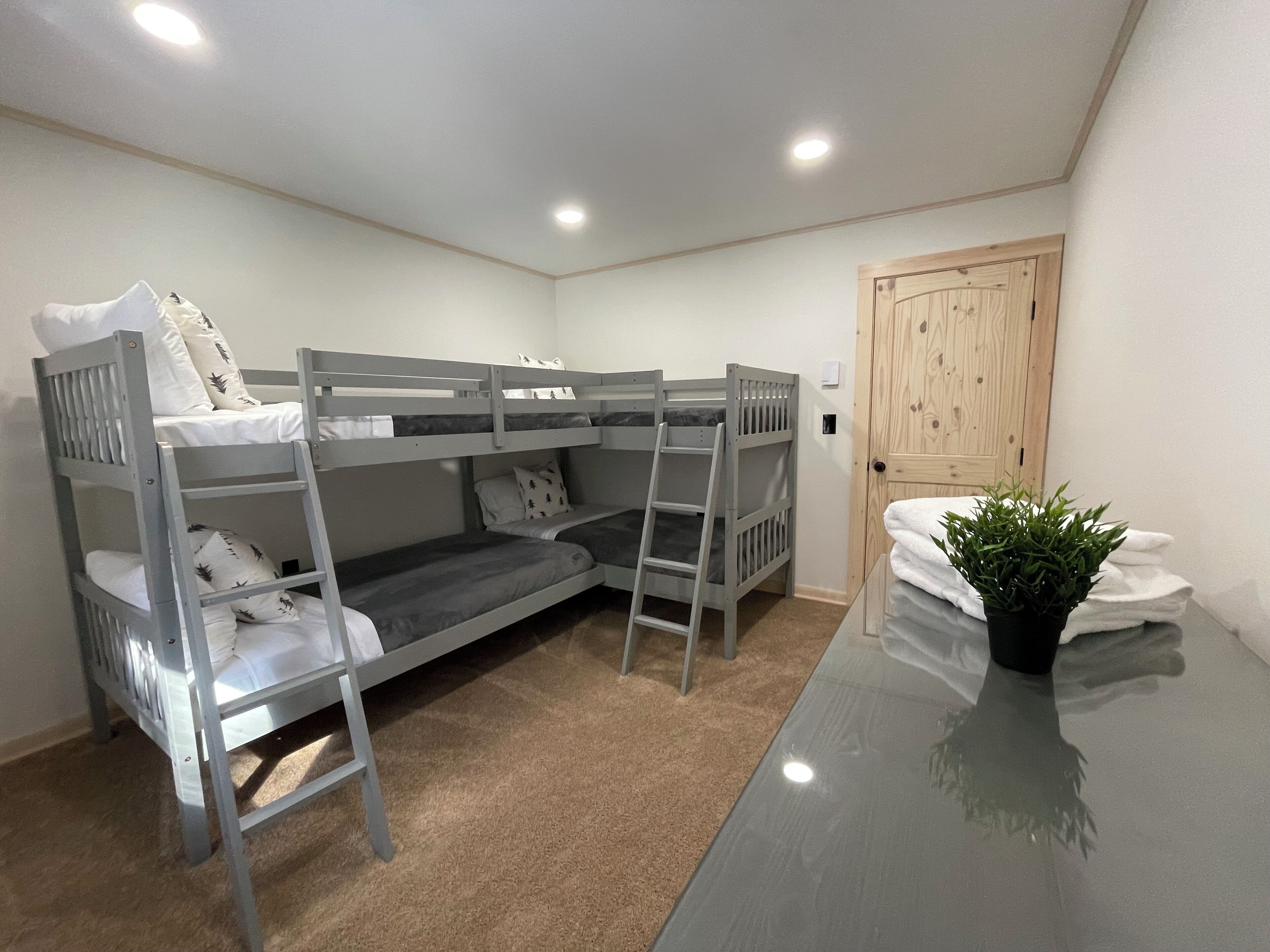 A bunk bed room with a wooden door, a small potted plant, and a glass table.