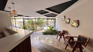 A reception area with a counter, wooden chairs, and a view of the outdoors. - Studio Toh 210 - Elle Residence (Tulum)