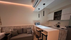 A compact living space with a sofa, a small kitchen area including a microwave and a coffee maker, and a bar stool. - Studio Toh 210 - Elle Residence (Tulum)