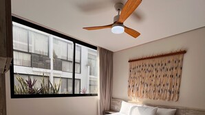 A modern bedroom with a large bed, a ceiling fan, a view of the outside, and a patterned rug. - Studio Toh 210 - Elle Residence (Tulum)