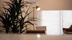 Ein modernes Wohnzimmer mit einer großen Pflanze, einem Sofa, einer Lampe und einem Fenster mit Jalousien.