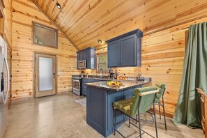 Una cocina con paredes de madera, una isla central con taburetes de bar, un microondas y un lavamanos.