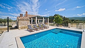Une piscine avec des chaises longues, un bâtiment en pierre et un ciel dégagé.